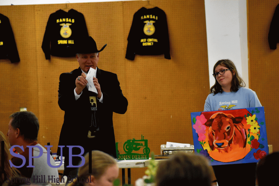 One item to be sold is a painting of a cow, made for and donated to the FFA. Jasmine Green, 10, holds the painting while the auctioneer accepts bids (Photo by A. Dickey).