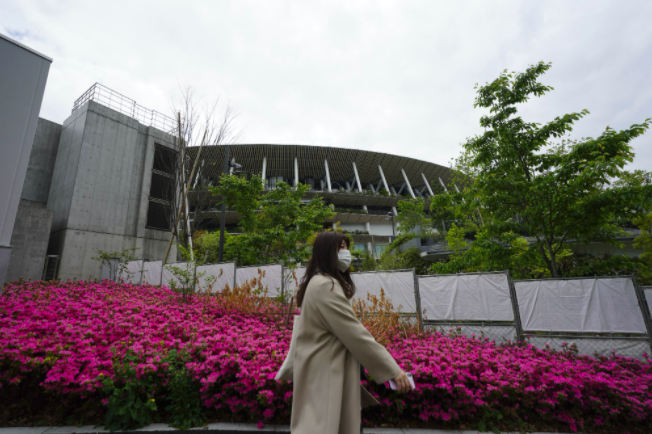 A woman walks past the Japan National Stadium, where all the festivities of the Olympics will take place (photo courtesy AP News).