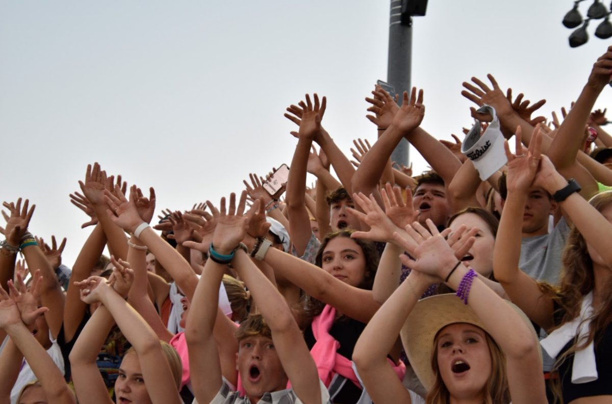 The students getting hyped up with making noise and jazz hands. Here they are cheering on their football team, hoping they take home the win (Photo by G. Cowsert). 