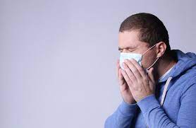 Person coughs into a tissue. Covering your mouth and staying home while sick will help stop the spread of illnesses. 