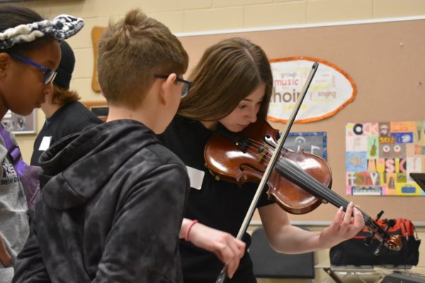 Alyssa Budd, 11, demonstrates their violin to Dayton Creek Elementary School students. The high school hosted groups of elementary students to observe band, orchestra, and choir (Photo by K.Tran). 