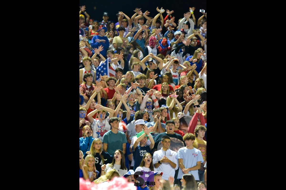 Students in the stands during a home football game against the Paola Panthers raise their hands before a kickoff Oct. 11.