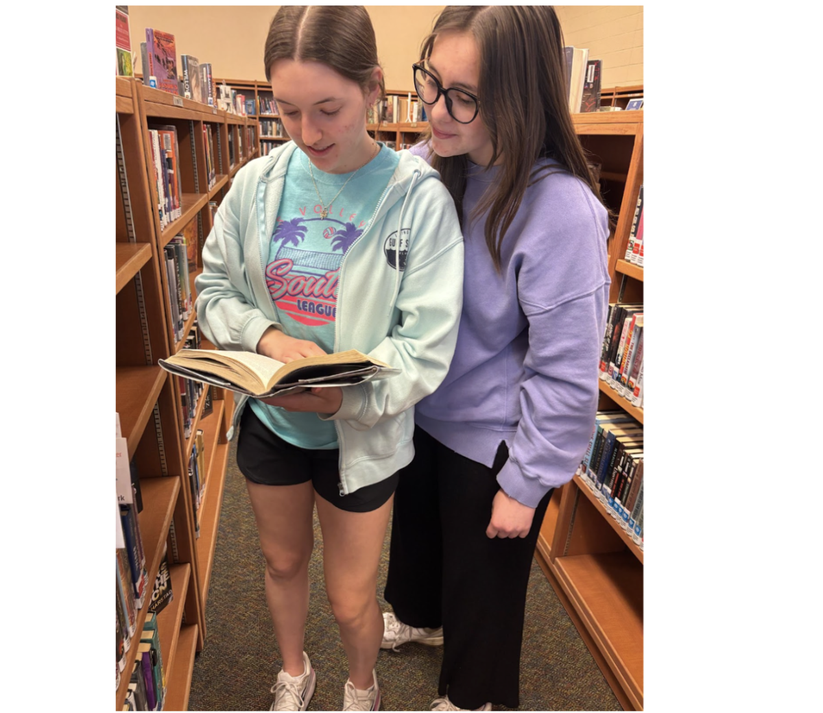 Norah McMains, 11, and Hannah King, 12 look at a book together deciding if they want to continue reading. (Photo illustration by Madi Brown)