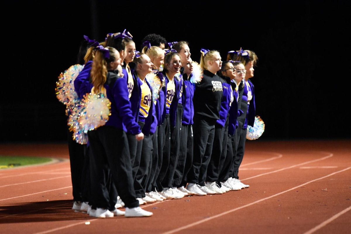The cheer team links arms and sways while the band plays the alma mater after a varsity football game.