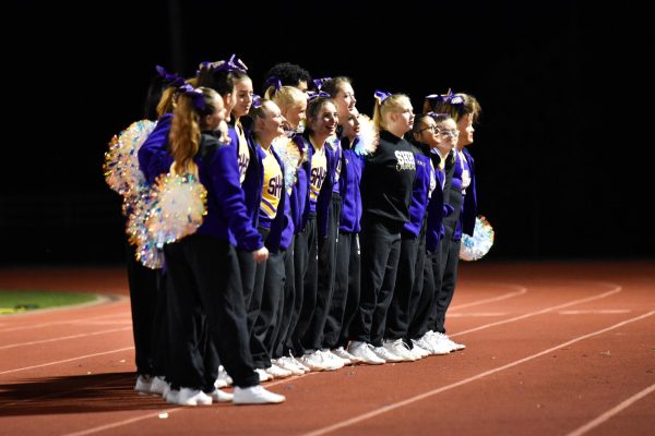 The cheer team links arms and sways while the band plays the alma mater after a varsity football game.