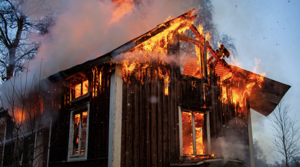 A house is engulfed in flames due to a fire. Smoke from the fire fill the air surrounding the house.