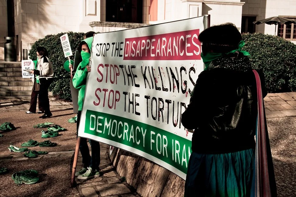 Two Iranian women hold a sign advocating for democracy in Iran. The establishment of a democracy in Iran has been a spoken goal of the U.S. military since the conflict began.