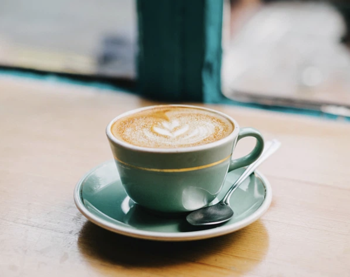 A warm latte sits in a ceramic cup, showcasing a cozy café atmosphere. The drink reflects the type of handcrafted coffee customers can expect at Apparition Coffee. 
